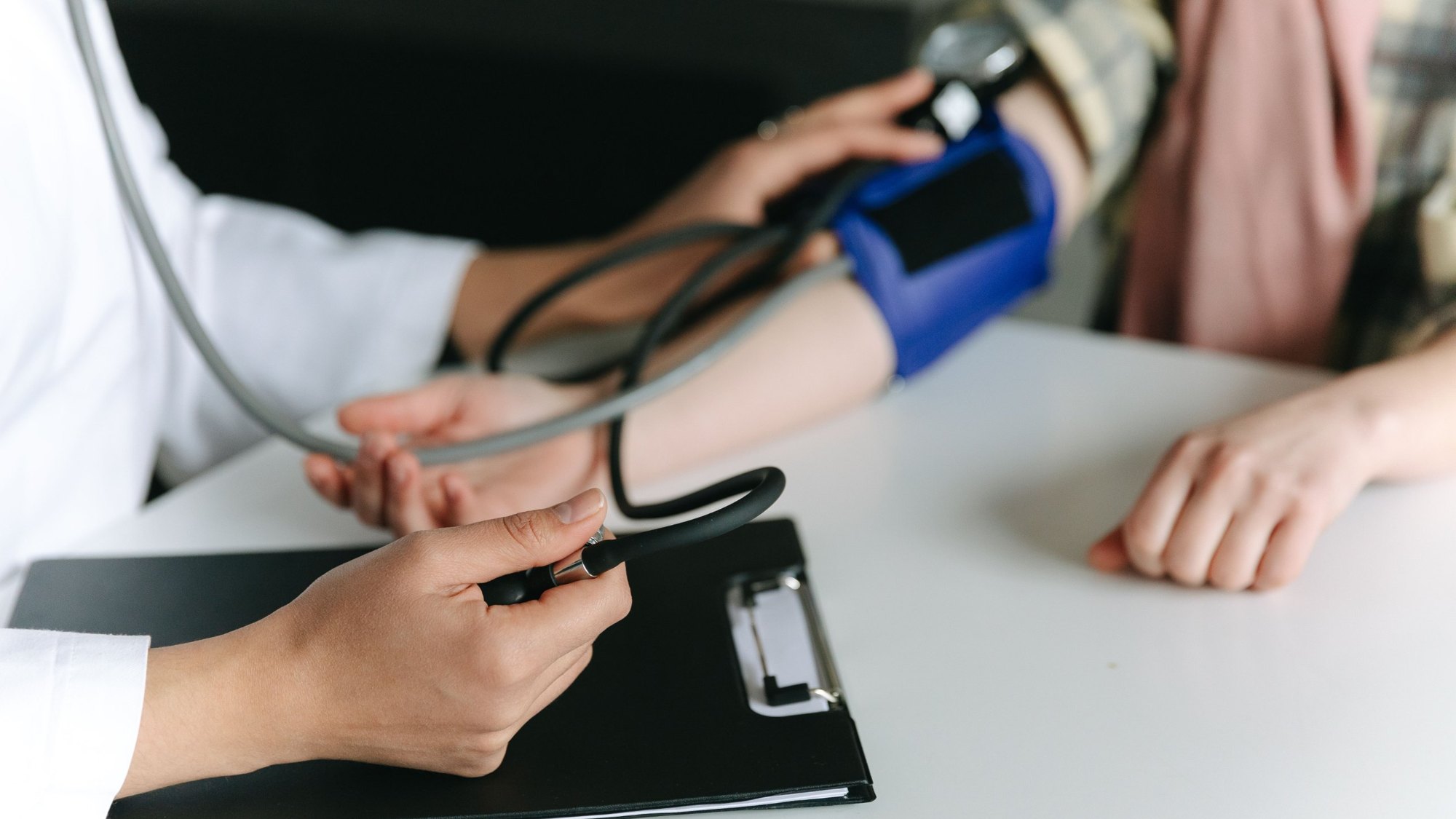 Clinician checking a patient's blood pressure beside a clipboard