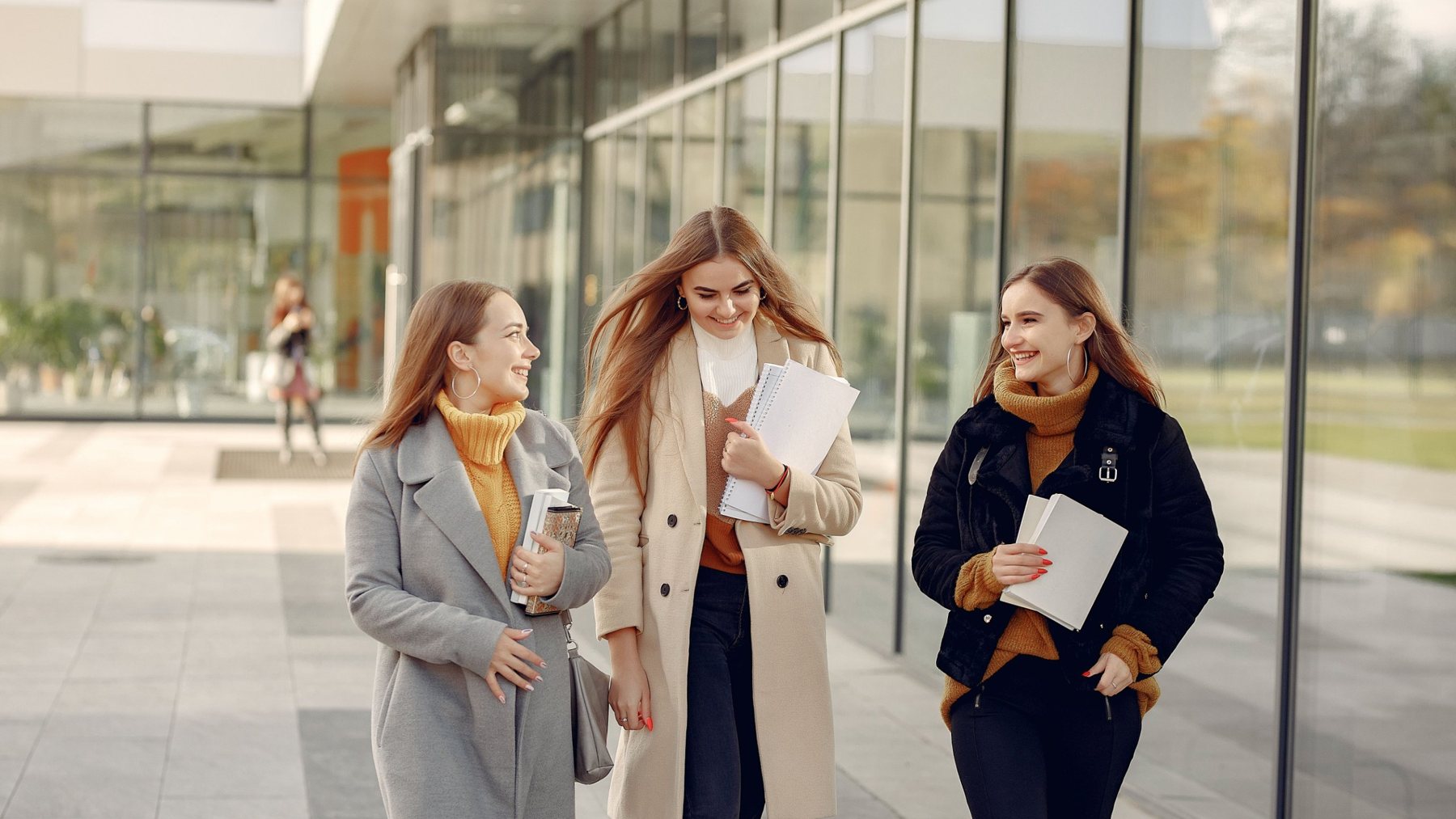 Three students walking on campus with notebooks